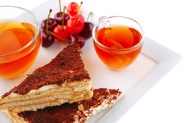 Two pieces of cake on a table with tea and cherries on a white background