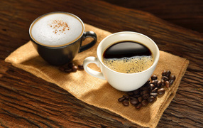 A cup of coffee and a cup of cappuccino on a table with coffee beans
