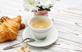 A cup of coffee and croissants on a table with white chrysanthemums