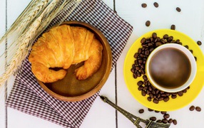A cup of coffee on a table with a fresh croissant