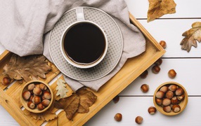 A cup of coffee on a table with hazelnuts and yellow leaves