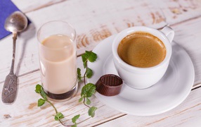A cup of coffee with chocolate candy and a glass of milk on a table