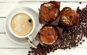A cup of coffee with cupcakes and coffee beans on the table