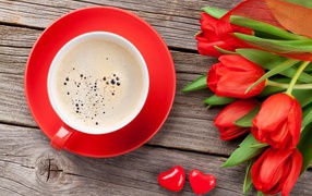 A cup of coffee with red tulips on a wooden table