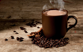 A cup of hot coffee with milk on a table with cinnamon and coffee beans