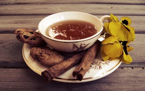 A cup of tea with cookies, cinnamon sticks and flowers