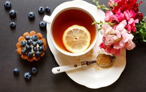 Чашка чая с лимоном на столе с кексом и цветами