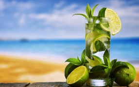 A glass of cold mojito on a table with mint and lime