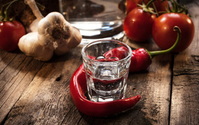 A glass of vodka on a table with red pepper and garlic