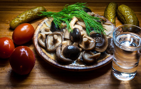 A glass of vodka on a table with salted mushrooms, tomatoes and cucumbers