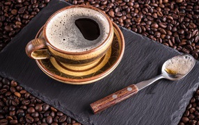 A large cup of coffee with a teaspoon is on coffee beans