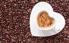 A white cup of coffee in the form of heart stands on coffee beans