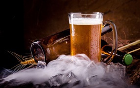 Бутылки пива с бокалом и кубиками льда на столе