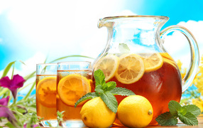 Холодный лимонад в графине на столе со стаканами и плодами лимона