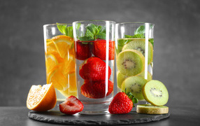 Напитки в стаканах с клубникой, киви и апельсинами на сером фоне