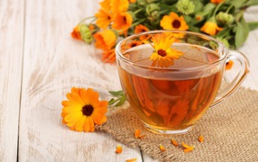 Стеклянная чашка чая с цветками календулы на столе