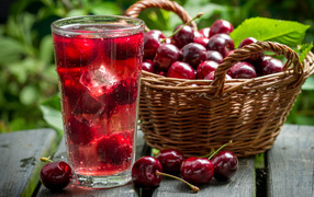 Glass of drink with ice on the table with a basket of sweet cherries