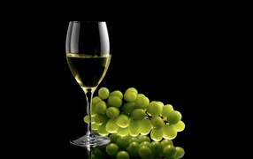 Glass of white wine with white grapes on a black background