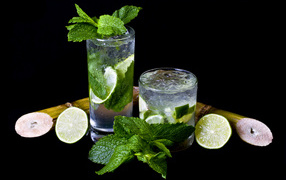 Mojito drink in glasses with lime and mint leaves on a black background