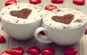 Two cups of coffee on a table with chocolate candies in the shape of a heart