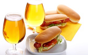 Two glasses of beer with hot dogs on a white background