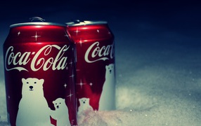Two red cans of Coca Cola drink are on the snow