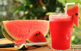 Watermelon drink in a glass on a table with a piece of watermelon