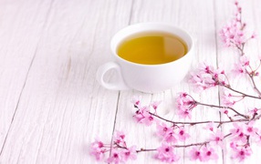 White cup of green tea on a table with pink flowers