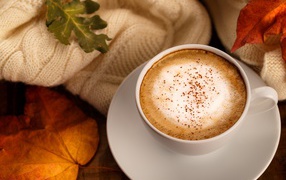 White cup with delicious coffee on the table with yellow leaves