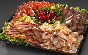 A large dish with appetizing meat cuts, lettuce and olives