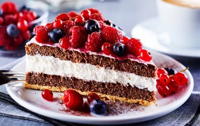 Аппетитный кусок торта на тарелке с ягодами малины, красной смородины и черники