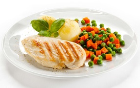 Chicken breast on a white plate with potatoes, carrots and green peas