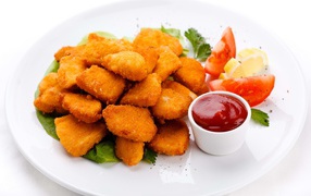 Chicken nuggets with sauce and tomatoes on a white plate