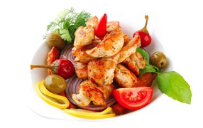 Жареные кусочки курицы на тарелке с овощами и зеленью 