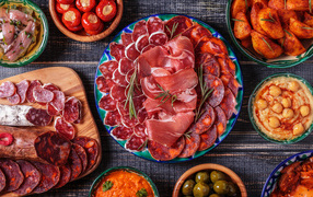 Большая тарелка с мясной нарезкой в центре праздничного стола