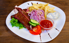 Meat with vegetables and french fries on a large white plate with sauce