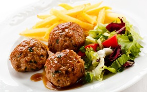 Meatballs with french fries and salad on a white plate