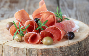 Prosciutto with olives on wooden table