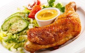 Жареная куриная ножка с овощами и соусом на тарелке