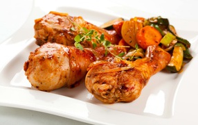 Roasted chicken legs with vegetables on a white background