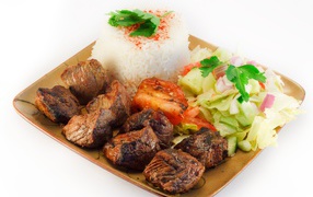 Шашлык с рисом и овощами в тарелке на белом фоне