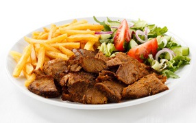 Кусочки мяса на тарелке с картофелем фри и салатом
