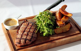 Steak on the board with potatoes, sauce and arugula