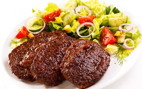 Три котлеты на тарелке с салатом на белом фоне