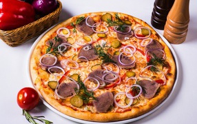 Delicious pizza with pickled cucumbers, tongue and onions on a table with vegetables