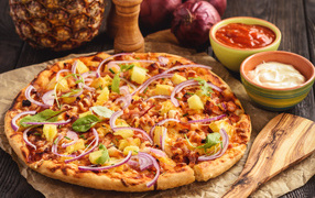 Пицца с ананасами и луком на столе с соусом