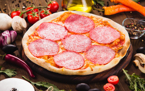 Pizza with salami on the table with vegetables