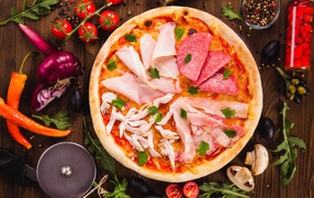 Pizza with sausage, chicken and slices of ham on a table with vegetables