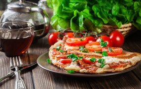 Pizza with tomatoes on the table with tea and herbs