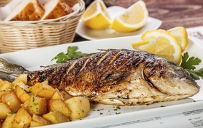 Baked fish on a plate with potatoes and lemon